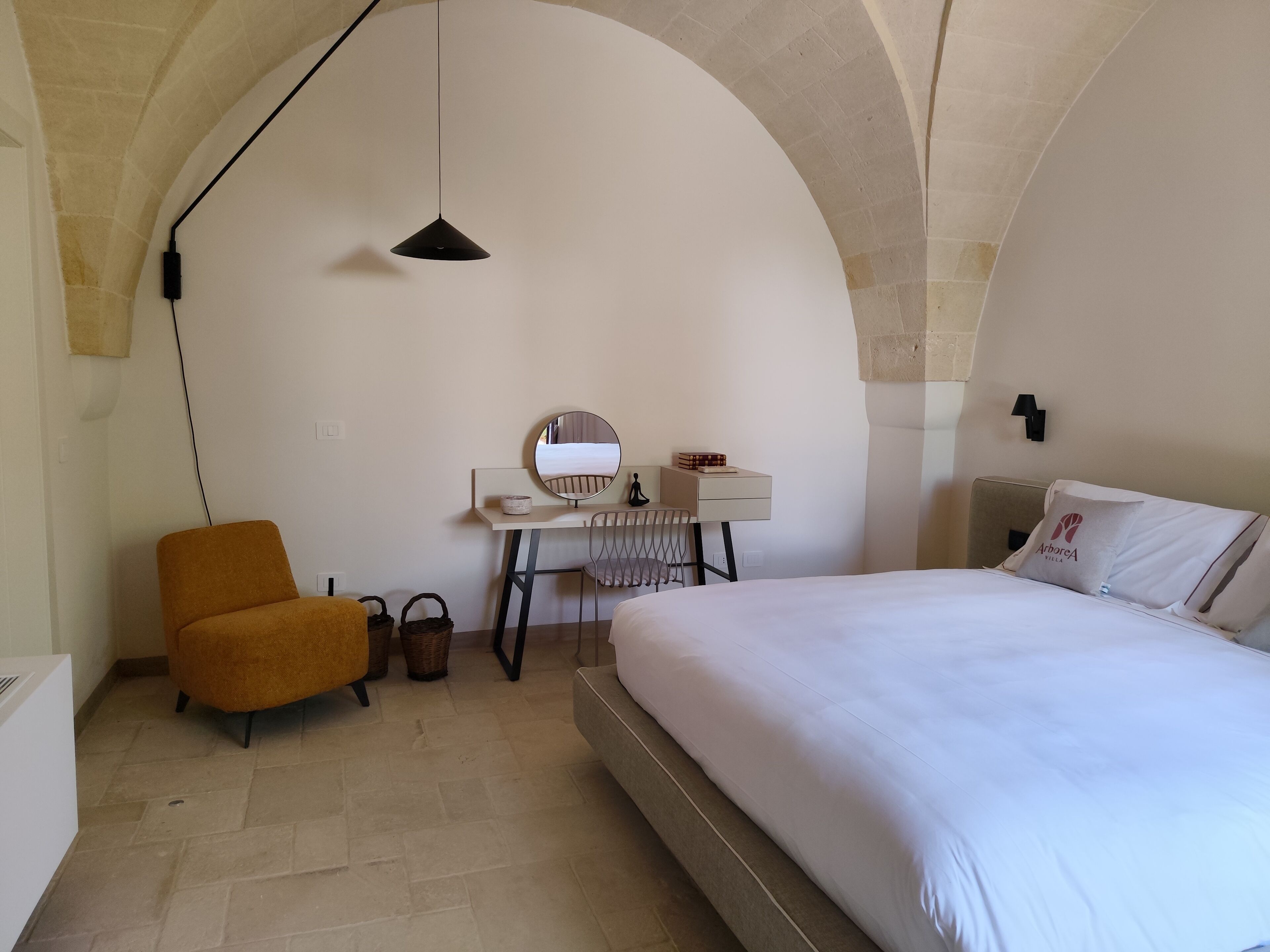 Una camera da letto con un letto, una scrivania con una sedia, una piccola poltrona arancione e una lampada a sospensione.