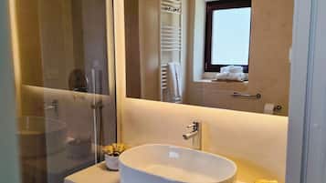 A modern bathroom with a large mirror, a white sink, a shower, and a towel rack.