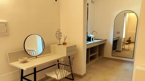 Uma casa de banho com toucador branco, espelho redondo, uma cadeira e um espelho grande refletindo uma cadeira e uma pia.
