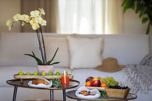 A dining area with a table set for breakfast, including fruits, pastries, and a glass of juice.
