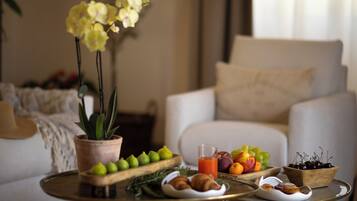 Un salon avec un canapé, une table basse sur laquelle sont disposés des fruits et des pâtisseries, et une plante en pot.