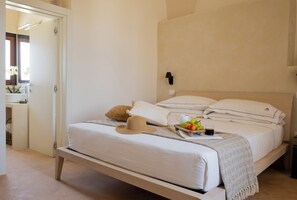 Un dormitorio con una cama, almohadas, un sombrero, una bandeja con fruta y una lámpara en la pared.
