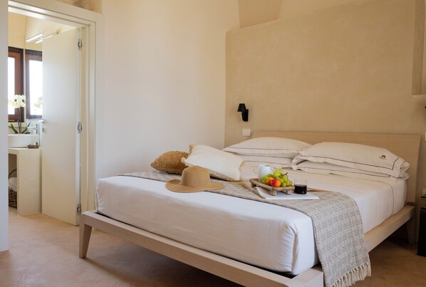 A bedroom with a bed, pillows, a hat, a tray with fruit, and a lamp on the wall.