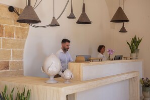 A reception desk with a stone wall backdrop, a potted plant, and a laptop.