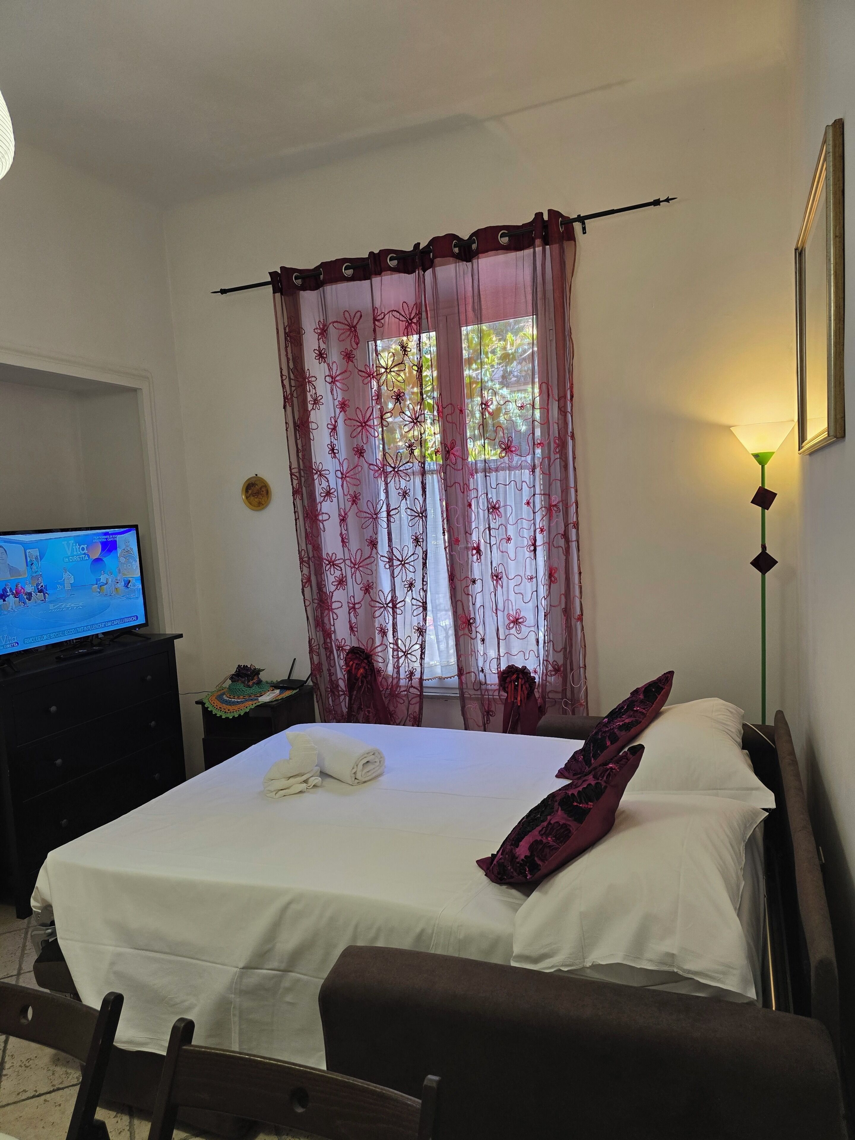 Quarto de hotel com cama, televisão, mesa de cabeceira e janela com cortinas.
