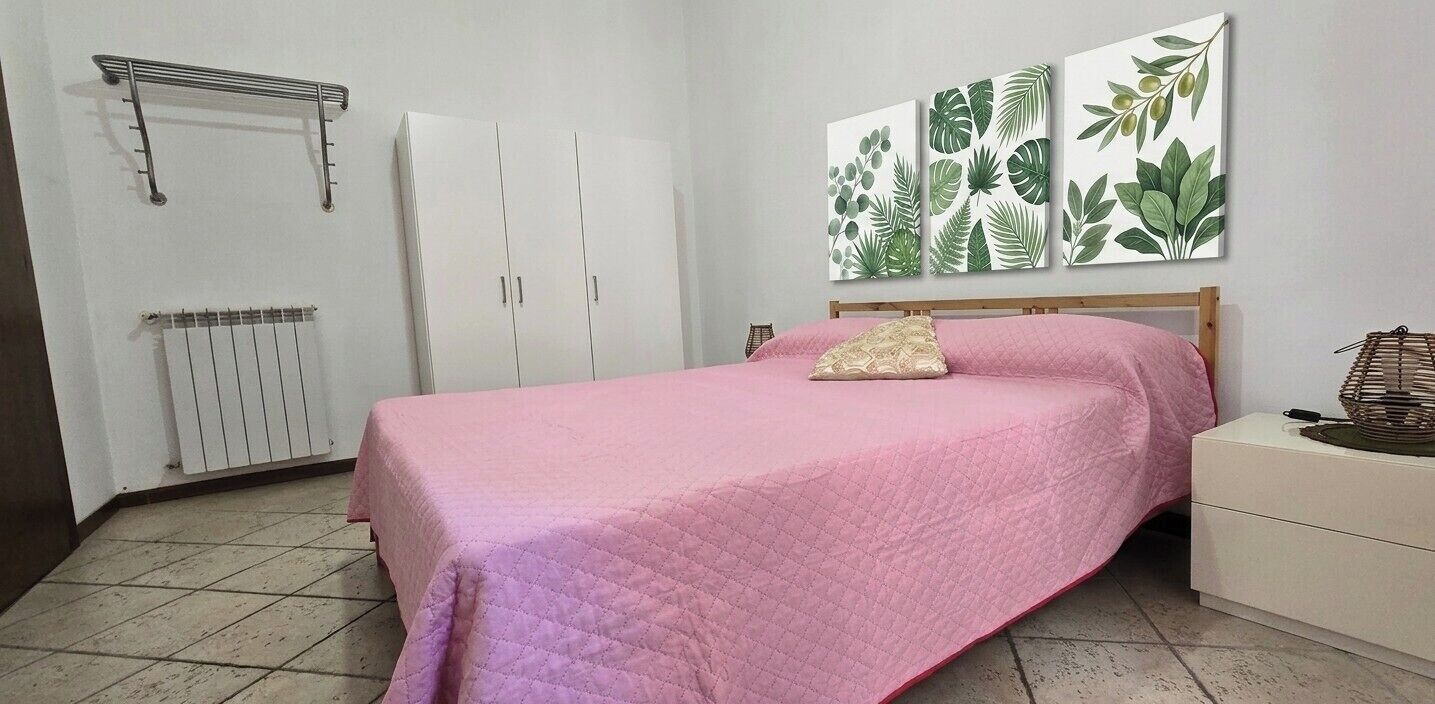 Ein Schlafzimmer mit Bett, Heizkörper, Kleiderschrank und einer Wand mit Pflanzenmotiven.