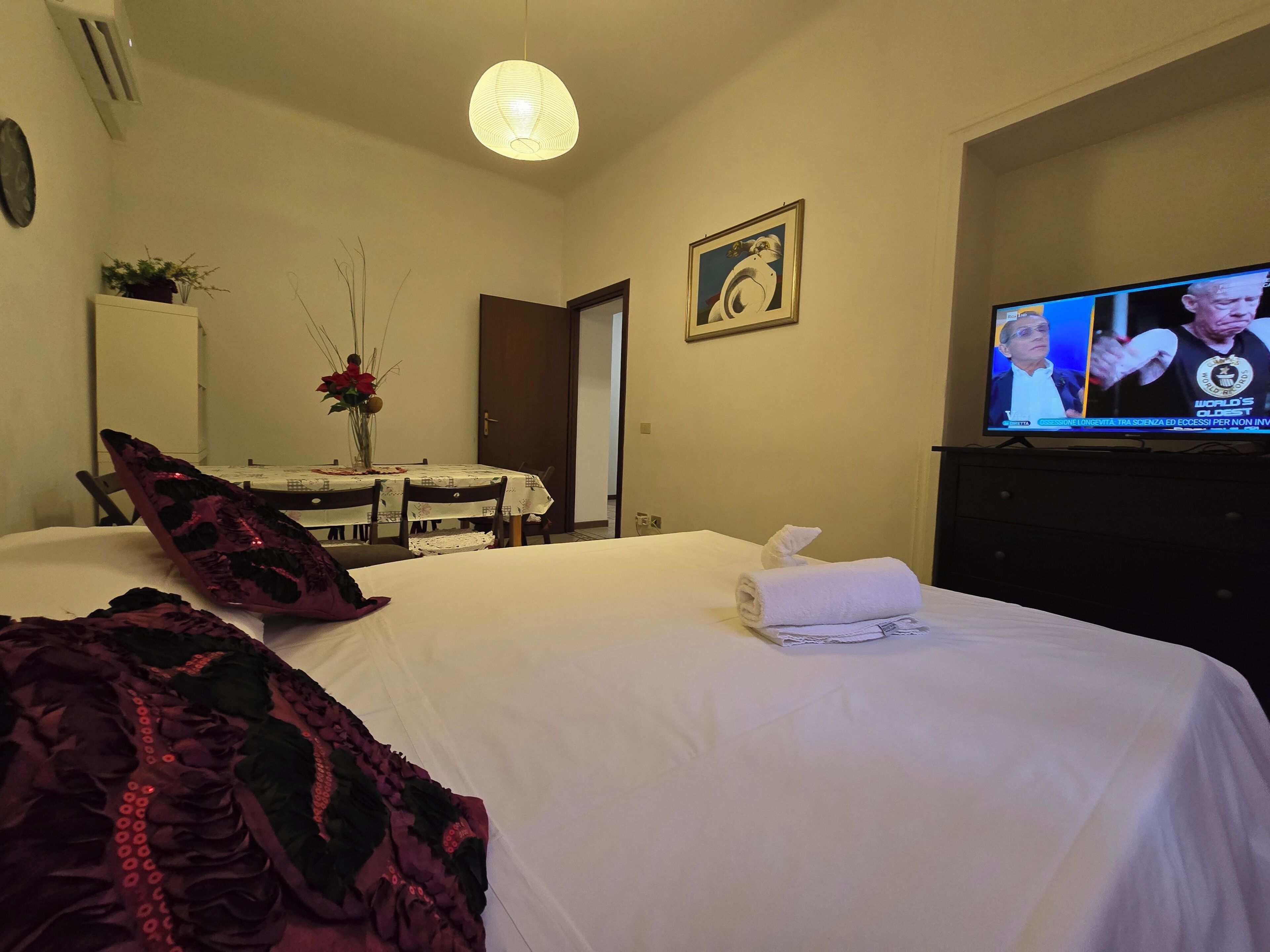 A hotel room with a bed, a television, a dining table with chairs, and a door.