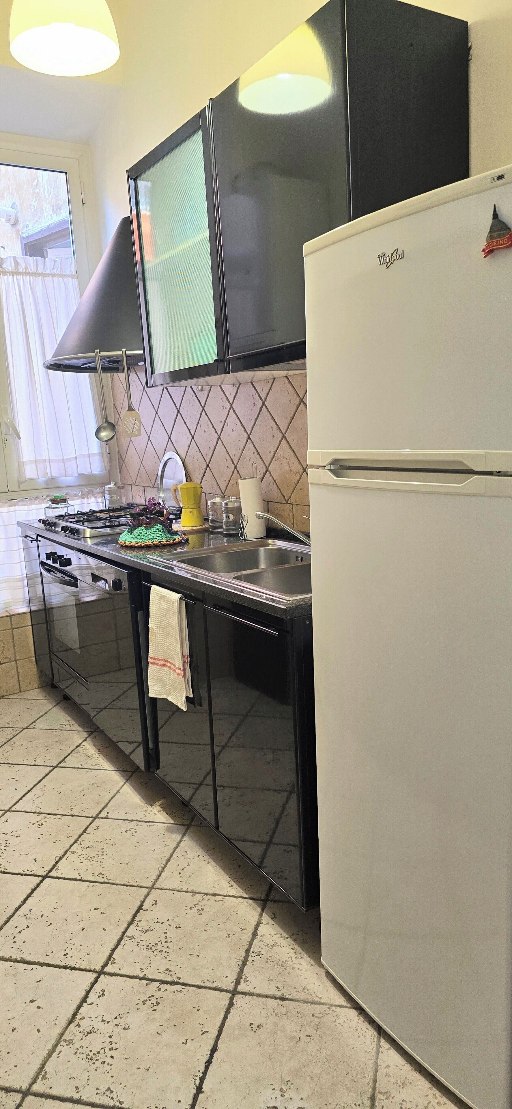 A kitchen with a gas stove, a sink, a refrigerator, and a window with curtains.