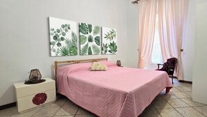 Un dormitorio con cama, mesita de noche, una silla y tres cuadros colgados en la pared.