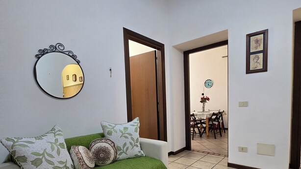 Una sala de estar con un sofá, un espejo y un comedor al fondo.