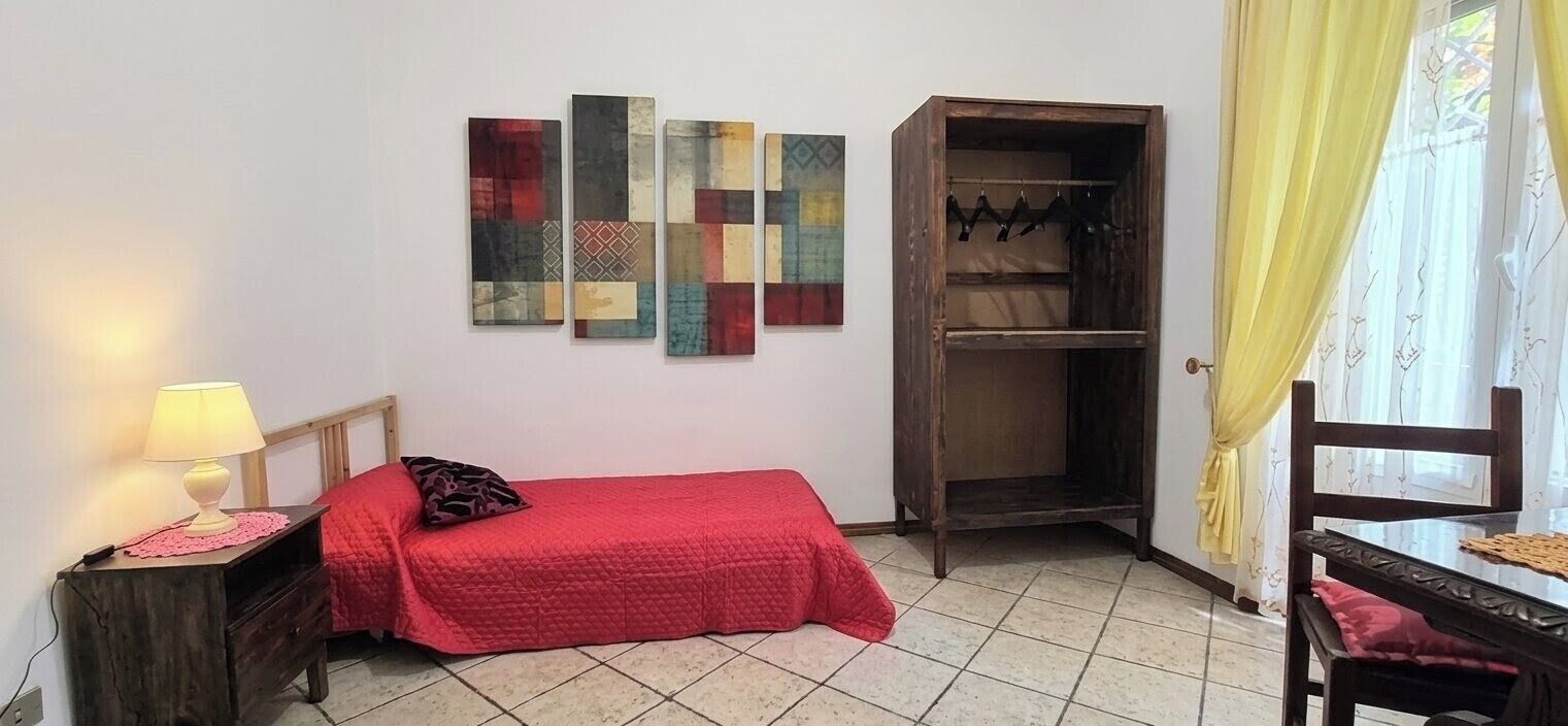 A bedroom with a bed, a nightstand, a wardrobe, and a wall with abstract art.