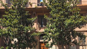 Un edificio de fachada marrón, con múltiples ventanas con contraventanas y una bandera en el balcón.