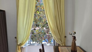 Una habitación con ventana, cortinas, una silla, una mesa y un florero con flores.