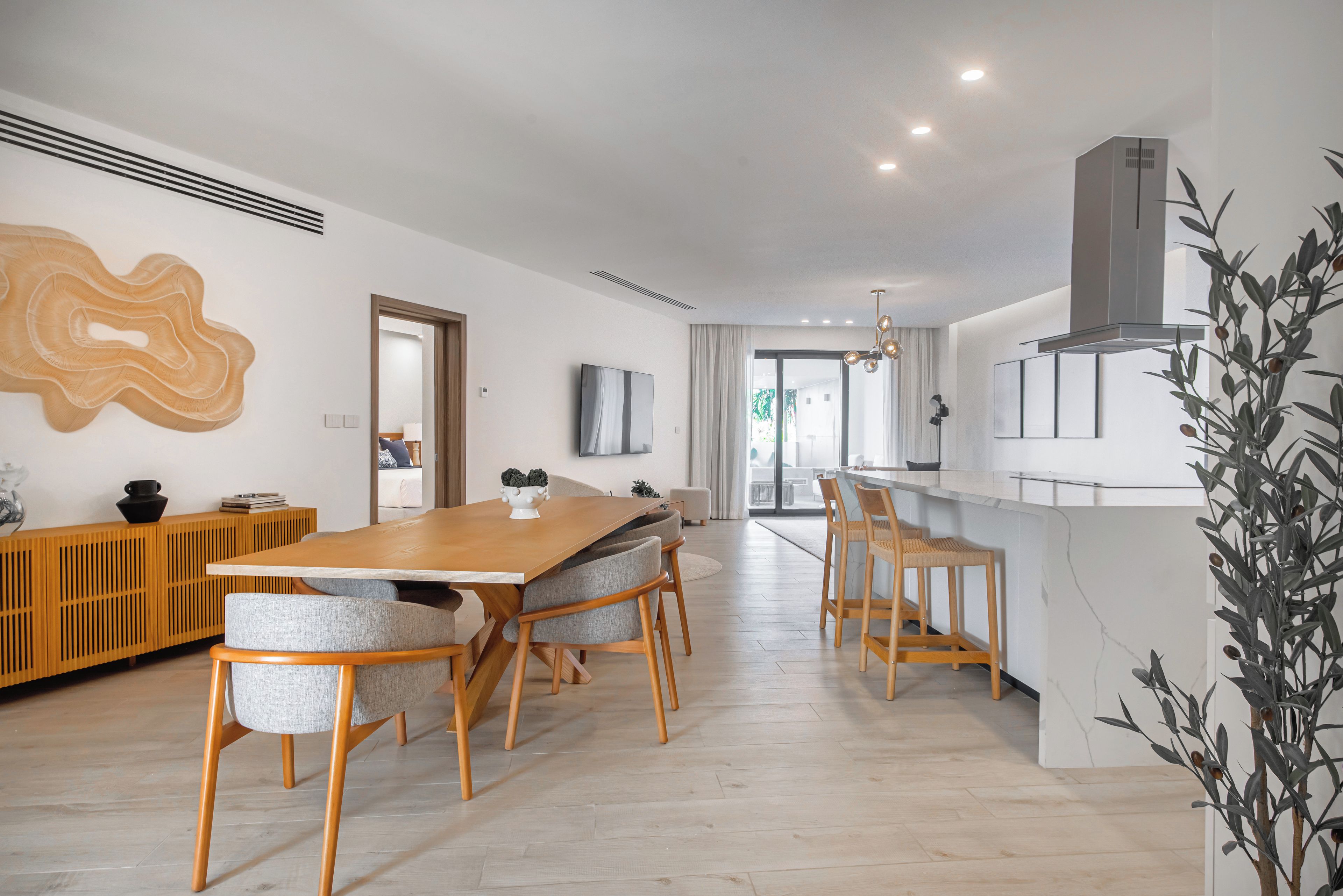 Uma área de refeições moderna com mesa e cadeiras de madeira, uma cozinha com fogão embutido e uma janela grande que proporciona iluminação natural.