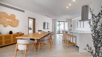 Uma área de refeições moderna com mesa e cadeiras de madeira, uma cozinha com fogão embutido e uma janela grande que proporciona iluminação natural.