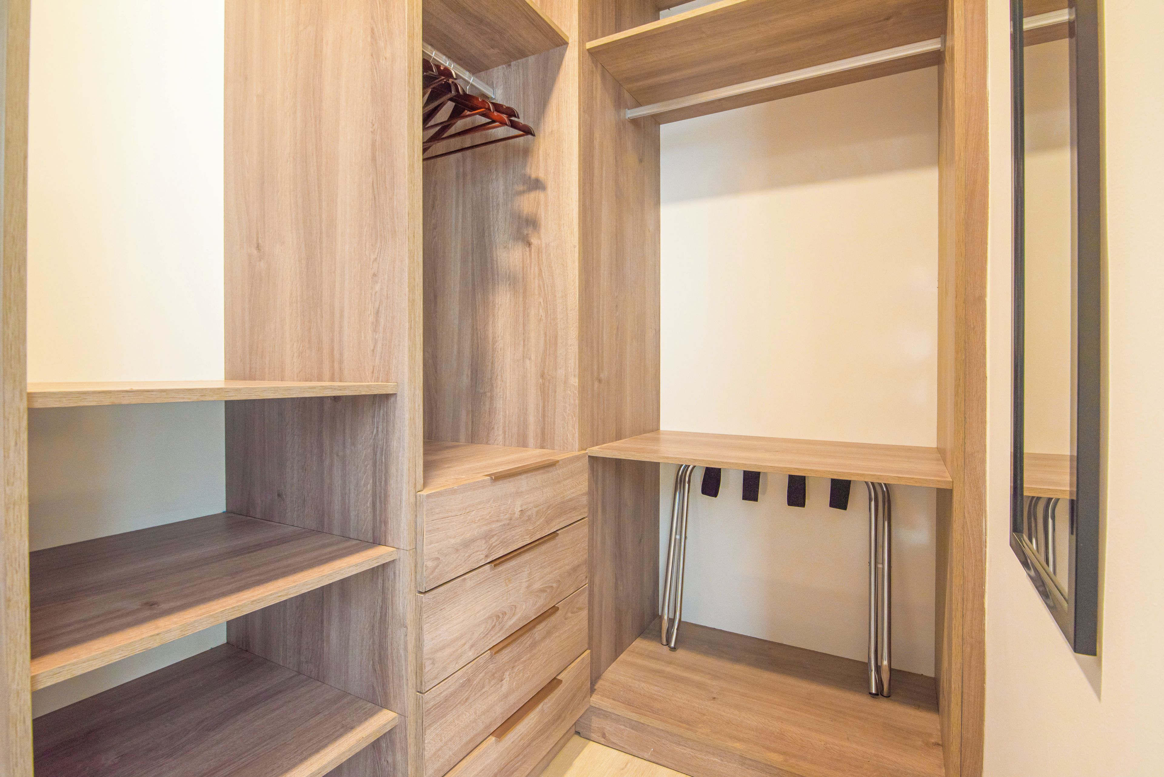 A wooden closet with multiple shelves and drawers, a hanging rod, and a mirror.