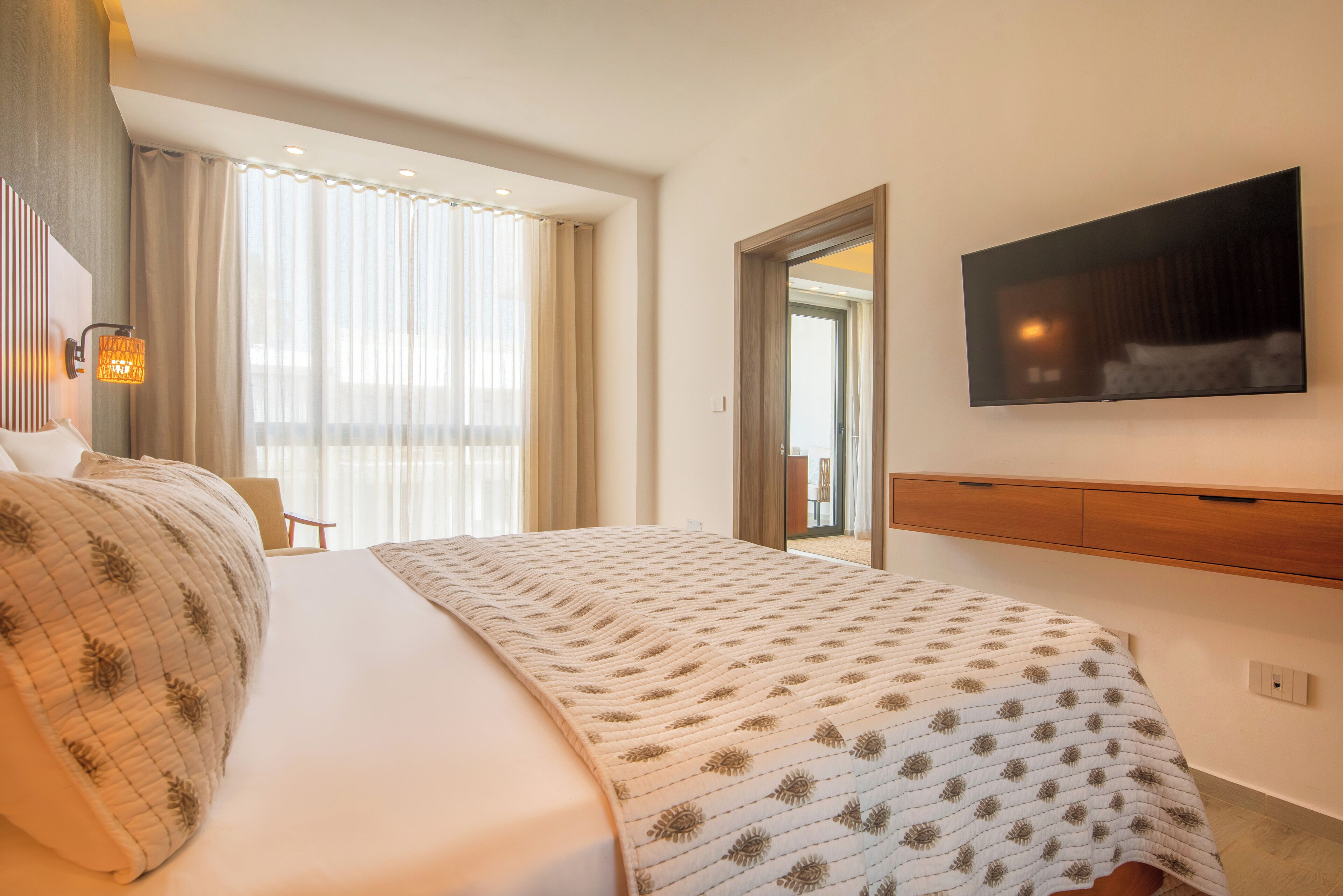 Una camera d'albergo con un letto grande, una televisione a schermo piatto montata a parete e una finestra con tende leggere.