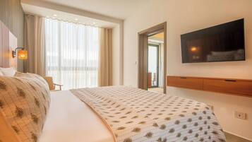 A hotel room with a large bed, a flat-screen TV mounted on the wall, and a window with sheer curtains.