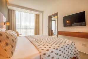 A hotel room with a large bed, a flat-screen TV mounted on the wall, and a window with sheer curtains. - Nivia Punta Cana Hotel & Residences (Punta Cana)