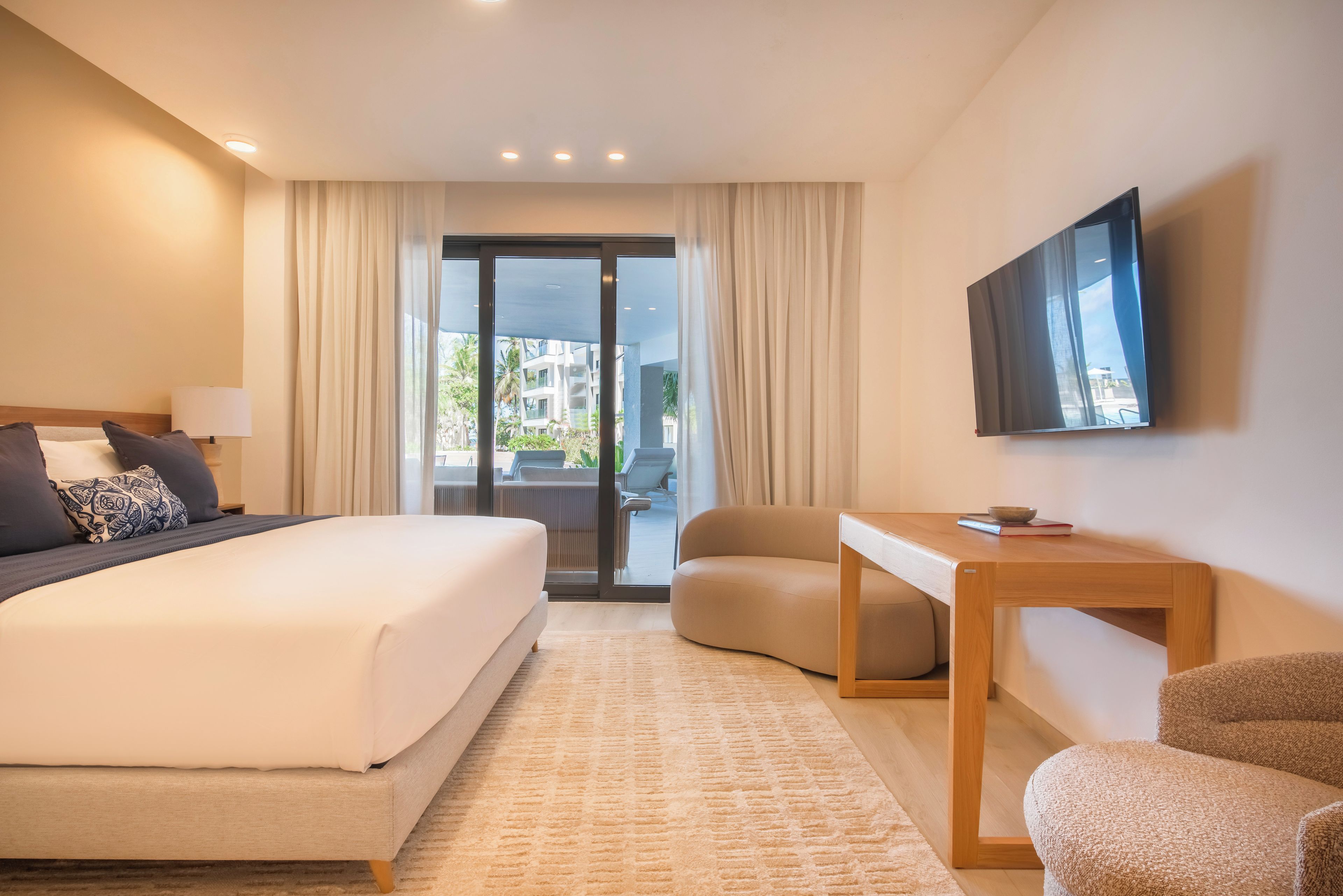 Ein Hotelzimmer mit einem Bett, einem Schreibtisch, einem Sessel, einem Fernseher und Blick ins Freie.