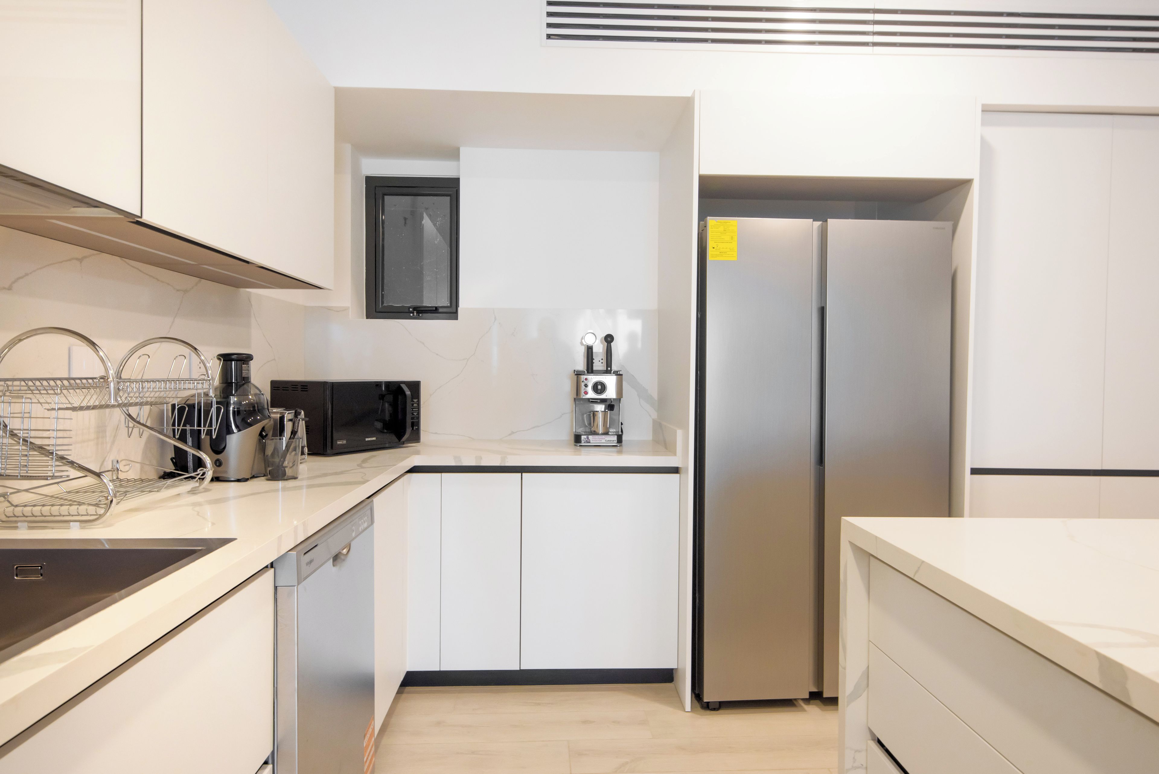 A modern kitchen with white cabinetry, a stainless steel refrigerator, a coffee maker, and a microwave.