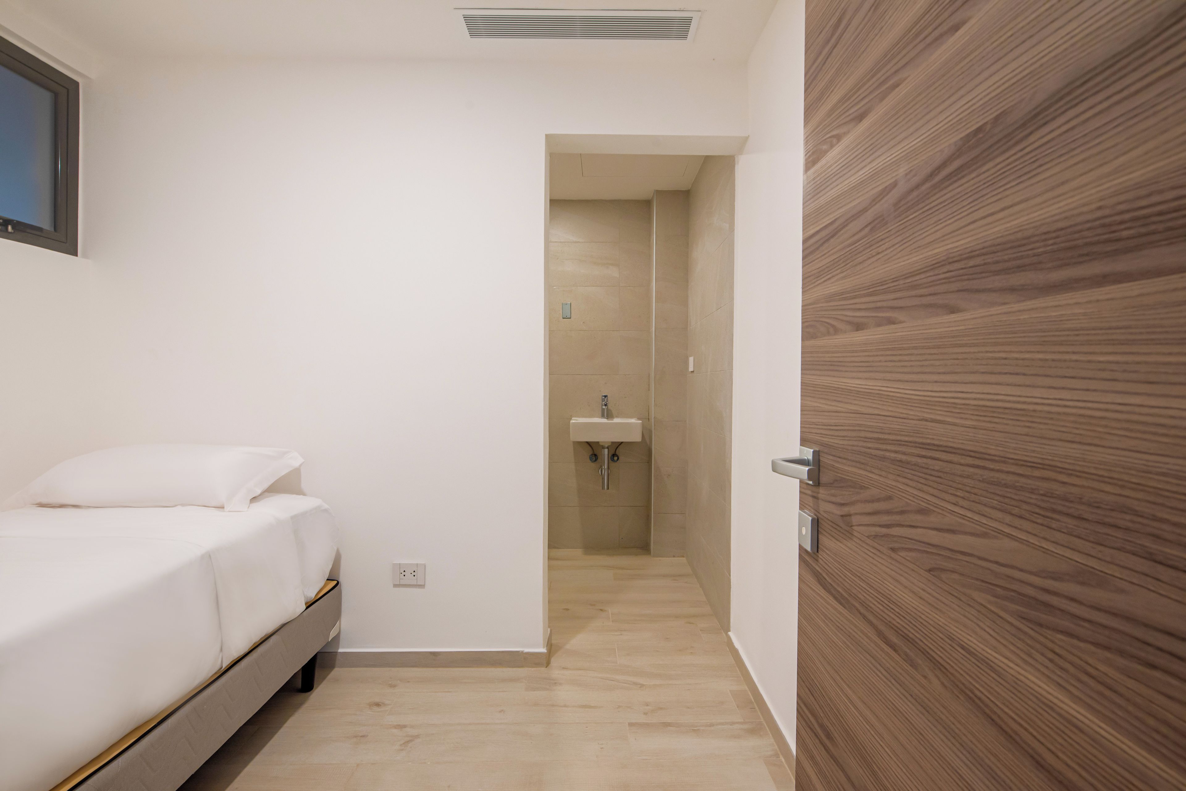 A bedroom with a bed, a wooden door, and a bathroom with a sink.