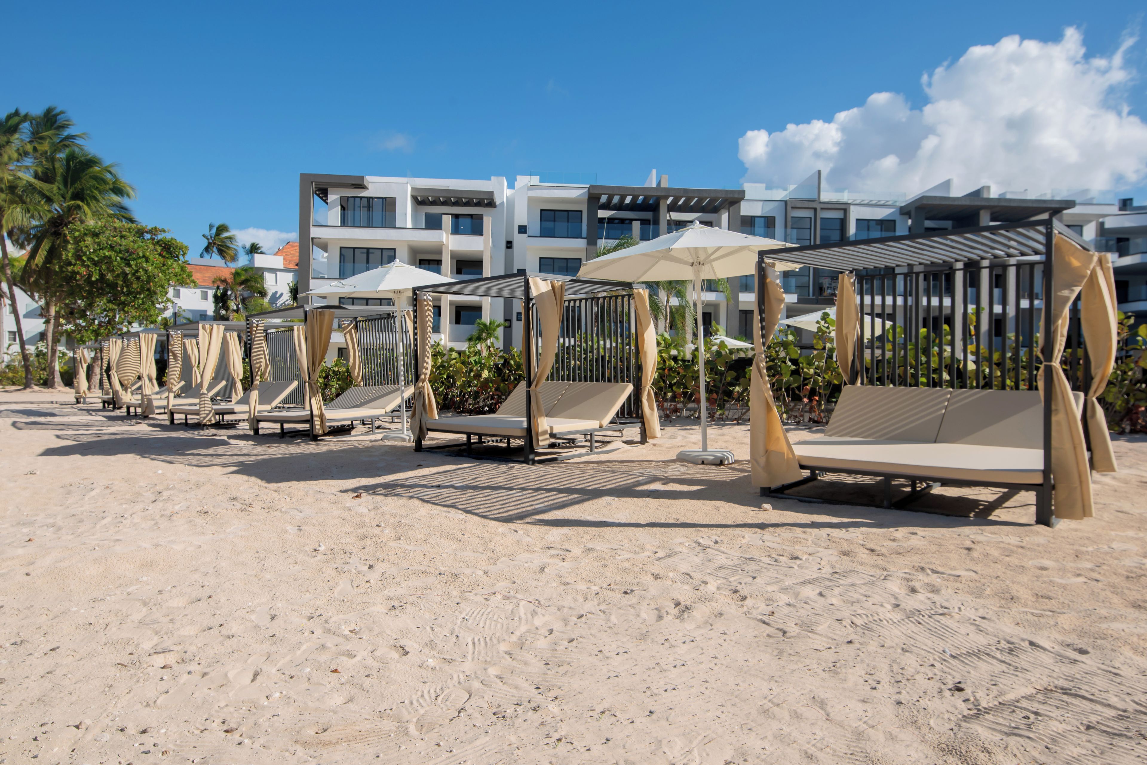 A beachside hotel with rows of sun loungers and umbrellas, a sandy beach, and modern buildings in the background.