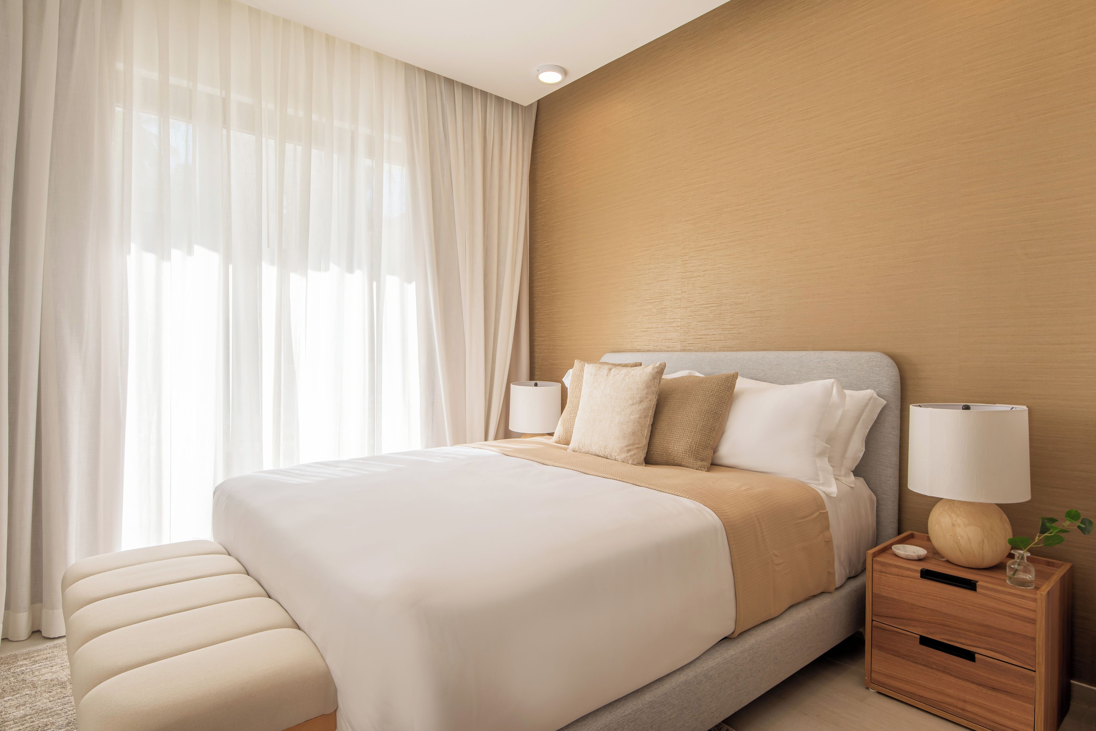 A hotel room with a large bed, bedside tables, a lamp, and sheer curtains.