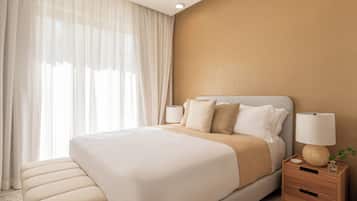 Een hotelkamer met een groot bed, nachtkastjes, een lamp en dunne gordijnen.