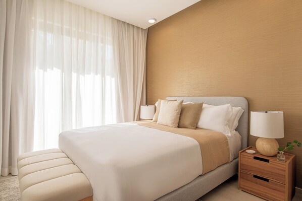 A hotel room with a large bed, bedside tables, a lamp, and sheer curtains. - Nivia Punta Cana Hotel & Residences (Punta Cana)