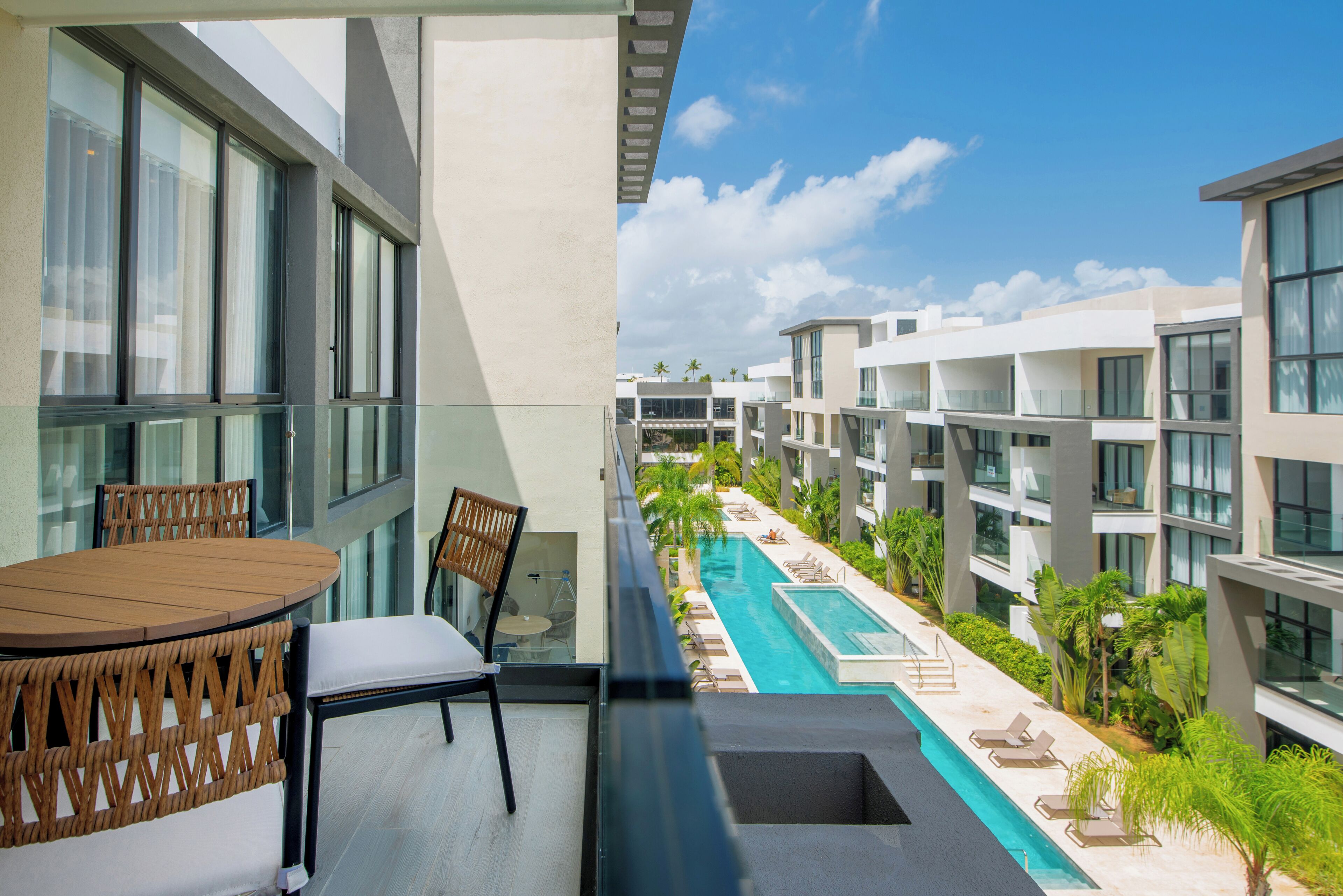 Ein Balkon mit Holztisch und -stühlen, mit Blick auf einen Swimmingpool und angrenzende Gebäude.