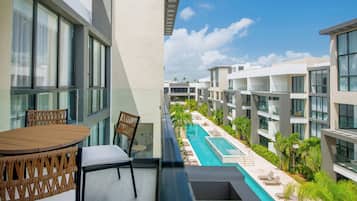 A balcony with a wooden table and chairs, overlooking a swimming pool and adjacent buildings.