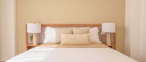 A neatly made bed with a wooden headboard, two bedside tables with lamps, and a vase with a plant on one of the tables.