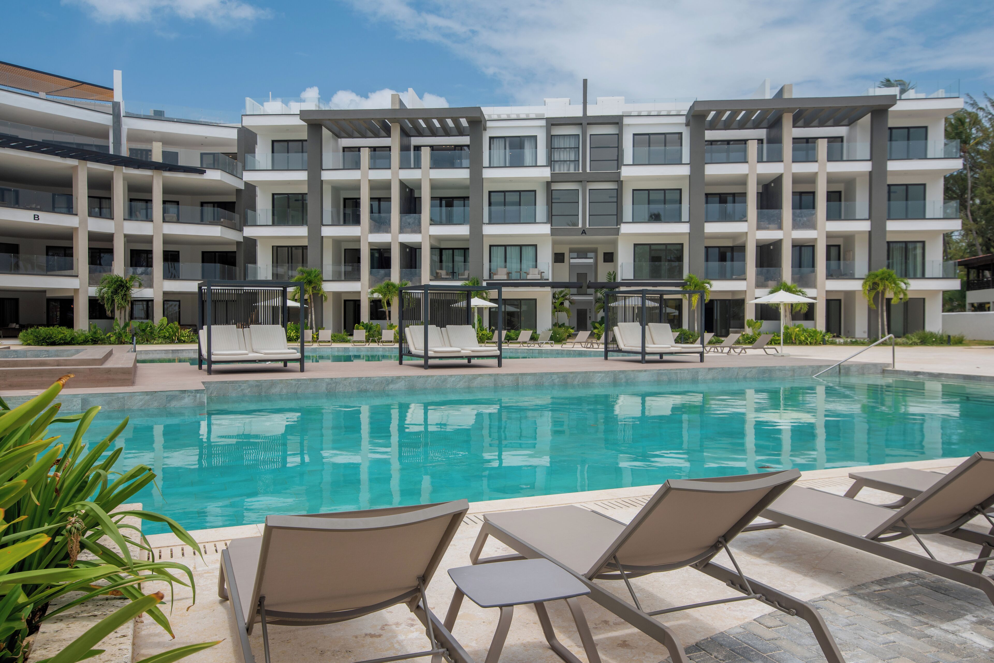 A modern hotel with a swimming pool, lounge chairs, and a multi-story building.