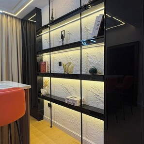 Um interior moderno com uma estante preta exibindo livros e objetos decorativos, piso de madeira e uma cadeira vermelha.
