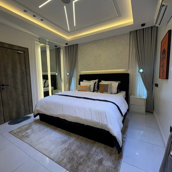 Quarto moderno com cama grande, mesas de cabeceira, espelho e luminária no teto.