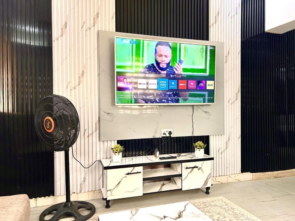 A modern living room with a flat-screen TV mounted on the wall, a marble-patterned entertainment unit below, and a standing fan to the left.
