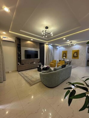 Uma sala de estar moderna com televisão de tela plana, um sofá, uma mesa de centro e um espaço de jantar com cadeiras amarelas.