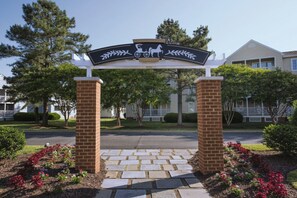 A residential entrance with a brick archway, a sign with a horse and carriage, and a paved driveway.