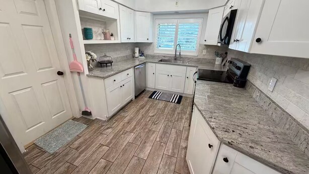 Een keuken met witte kastjes, een granieten aanrechtblad, een spoelbak en een raam met jaloezieën.