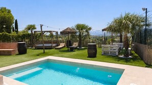 A rectangular swimming pool with a tiled edge, surrounded by a grassy area with palm trees and a wooden pergola. - Country House 'Burraca Oasis En Cartama' with Mountain View, Private Pool and Private Terrace (Cártama)
