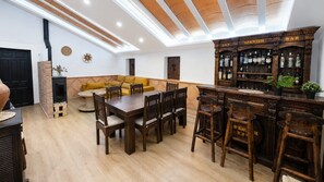 Een gezellige woonkamer met een houten eettafel, een geel sofa en een barhoek met houten planken.