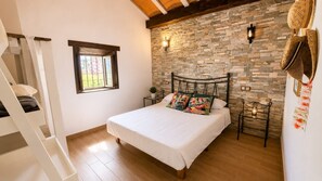 A bedroom with a bed, a window, a stone wall, and a wooden floor. - Country House 'Burraca Oasis en Cártama' with Mountain View, Private Pool and Terrace (Cártama)