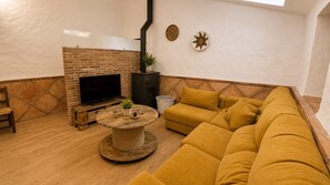 A cozy living room with a brick fireplace, a round wooden coffee table, a mustard-colored sofa, and a television. - Country House 'Burraca Oasis en Cártama' with Mountain View, Private Pool and Terrace (Cártama)