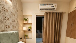 Quarto com cama, mesa de cabeceira, luminária, planta em vaso, aparelho de ar condicionado e guarda-roupa.