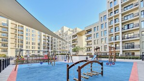A playground with swings, slides, and climbing structures, surrounded by apartment buildings. - Bloomfields Studio in Hayat Boulevard  (Dubai)