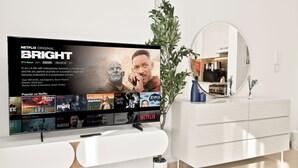 A modern living room with a flat-screen TV displaying a Netflix show, a white cabinet, a mirror, and a potted plant. - Bloomfields Studio in Hayat Boulevard  (Dubai)