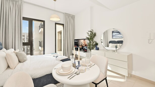 A modern hotel room with a bed, a dining table set with plates and cutlery, a round mirror, and a television. - Bloomfields Studio in Hayat Boulevard  (Dubai)