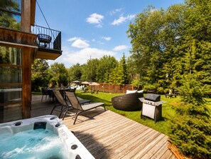 Une terrasse en bois avec un jacuzzi, un coin salon extérieur et un barbecue.