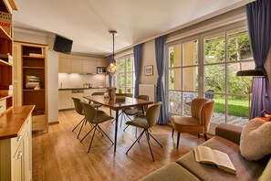 A modern living room with a wooden dining table, comfortable seating, and a large window with curtains.